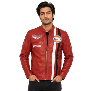 Pode incluir: Casaco de couro vermelho com zíper preto, com uma faixa branca e preta na lateral. Os patches incluem "HEUER", "Firestone" e um logotipo "Gulf". O casaco tem um design clássico e desportivo.