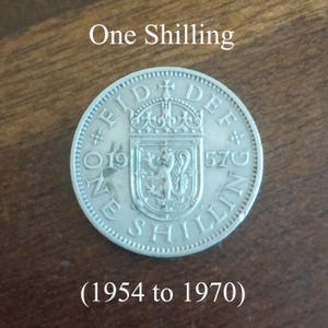 May include: A silver One Shilling coin from 1957, with text reading "One Shilling" and "(1954 to 1970)". The coin features a crowned shield with a lion and other details.