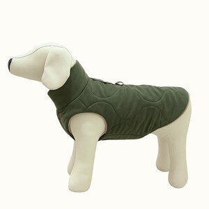 May include: Olive green quilted dog vest with a high collar and a circular ring detail. The dog coat is designed to fit a dog's body shape and is made of a soft, padded material. The vest is displayed on a white dog mannequin.