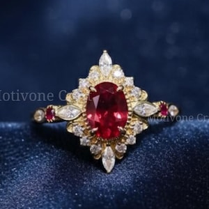 May include: A gold ring with a large oval ruby center stone, surrounded by smaller white and red gemstones. The ring has an ornate design and is set against a dark blue fabric. The text "Motivone Craft" is visible.