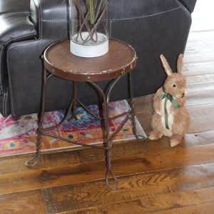 May include: A black leather sofa with a vase of white flowers and pink pom-poms on a small wooden table with a metal base. A brown stuffed rabbit sits on the floor next to the table.