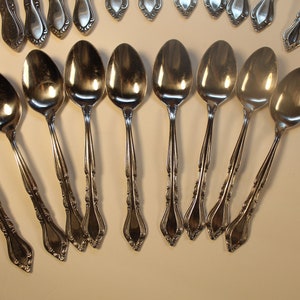 May include: A set of silver spoons with ornate handles. The spoons are arranged in a fan shape on a white surface.