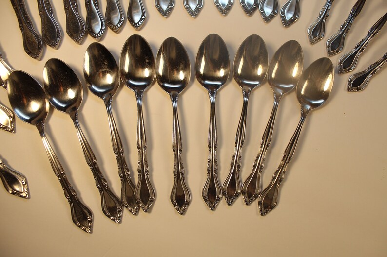 May include: A set of silver spoons with ornate handles. The spoons are arranged in a fan shape on a white surface.