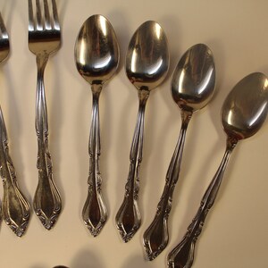 May include: A set of silver flatware, including forks and spoons, with ornate handles. The flatware is arranged on a white surface.