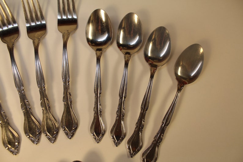 May include: A set of silver flatware, including forks and spoons, with ornate handles. The flatware is arranged on a white surface.