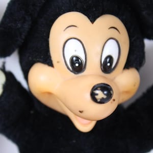 May include: Vintage Mickey Mouse plush toy with black fur, a tan face, and white gloves. The toy has large black eyes and a black nose. The plush is in a classic pose with arms outstretched.