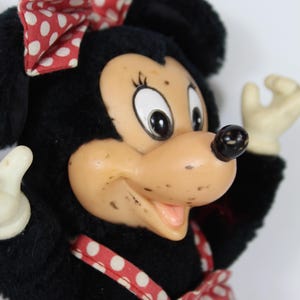 May include: A vintage Minnie Mouse plush doll with a black plush body, a tan face, and a red and white polka dot bow and dress. The doll has white gloves and a black nose. The doll is a classic Disney character.