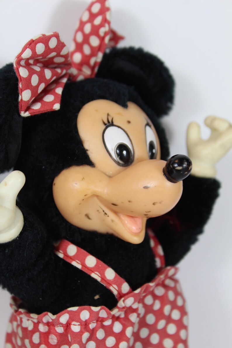 May include: A vintage Minnie Mouse plush doll with a black plush body, a tan face, and a red and white polka dot bow and dress. The doll has white gloves and a black nose. The doll is a classic Disney character.