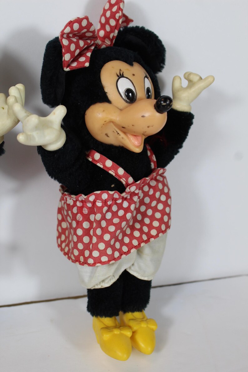 May include: A vintage Minnie Mouse plush doll. The doll has a black plush body, a red and white polka dot bow and skirt, and yellow shoes. The face is made of a tan plastic material with black eyes and a black nose.