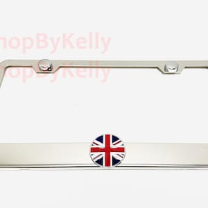 May include: A shiny chrome license plate frame with a Union Jack emblem. The frame has a rectangular shape with rounded corners and two chrome fasteners at the top. The emblem is a circular design with the British flag.
