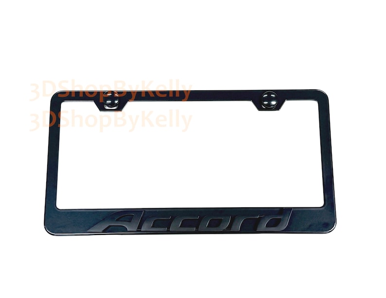 May include: A black rectangular license plate frame featuring the word Accord embossed in a matching black font along the bottom edge. The frame includes two circular mounting holes at the top with integrated black hardware caps for installation.