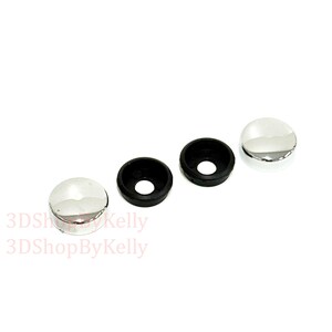 May include: Two circular chrome-finished screw covers with smooth, reflective surfaces and two corresponding black plastic washers with central holes. The text 3DShopByKelly is visible in light red lettering on the lower left side of the image.