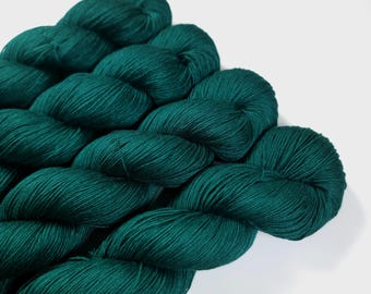 May include: Close-up of several skeins of teal-colored yarn. The yarn is tightly wound and has a soft, textured appearance. The skeins are arranged in a diagonal pattern, with the light reflecting off the fibers. This yarn is suitable for knitting and crochet projects.