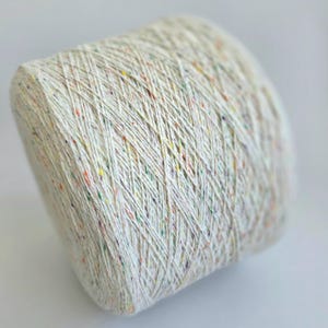 May include: A large, tightly wound spool of off-white yarn with colorful flecks of red, yellow, green, and purple. The yarn is tightly spun, creating a textured surface. Ideal for knitting, crocheting, or other fiber crafts.