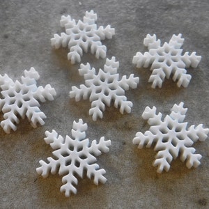 May include: Six white snowflake-shaped ornaments. The snowflakes are made of a lightweight material and have a delicate, intricate design.