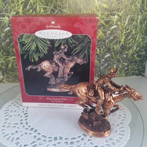 May include: A bronze-colored Hallmark Keepsake ornament depicting a Pony Express Rider on horseback. The ornament is part of the New Collector's Series and features the text "Pony Express Rider The Old West".