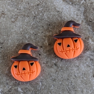 May include: Two orange pumpkin-shaped decorations with black triangle eyes and stitched mouths. Each pumpkin wears a brown witch hat with an orange band. These Halloween-themed decorations are perfect for crafts or seasonal decor.