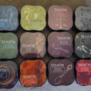 May include: Twelve ink pads in a variety of colors and designs. Each pad has the word "StazOn" printed on it, along with the color name and a design. The ink pads are arranged in a 4x3 grid.