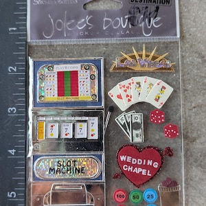 May include: A sheet of stickers with a Las Vegas theme. Includes slot machines, playing cards, dice, casino chips, and a heart-shaped "Wedding Chapel" sticker. The stickers are in various colors, including red, gold, and green.