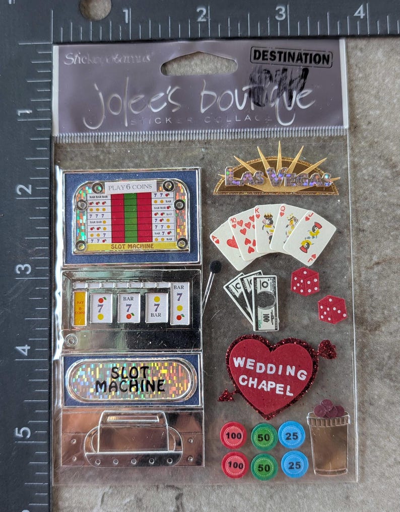 May include: A sheet of stickers with a Las Vegas theme. Includes slot machines, playing cards, dice, casino chips, and a heart-shaped "Wedding Chapel" sticker. The stickers are in various colors, including red, gold, and green.
