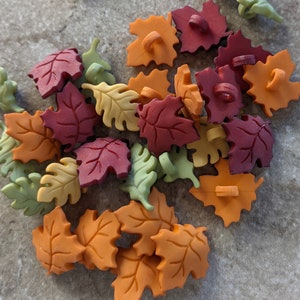 May include: A collection of leaf-shaped buttons in various autumn colors, including orange, red, yellow, and green. The buttons have a detailed leaf vein design and a loop on the back for sewing. These decorative buttons are ideal for craft projects.
