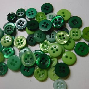 May include: A collection of green buttons in various sizes and shades. The buttons are arranged in a circular pattern on a white surface.