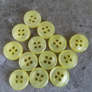 May include: A collection of 12 yellow plastic buttons with four holes each. The buttons are arranged in a triangular shape.
