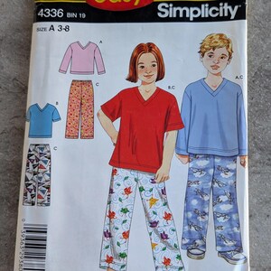 May include: A Simplicity sewing pattern for children's pajamas, size A 3-8. The pattern features illustrations of pajama sets with various designs, including floral and airplane prints. The packaging has the text "IT'S SO easy" and "Simplicity".