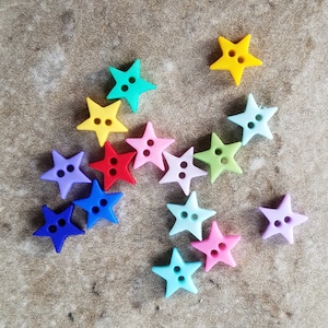 May include: Assortment of 13 colorful star-shaped buttons in various shades of blue, green, yellow, red, and pink. The buttons are made of silicone and have two holes each.