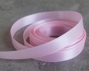 May include: A roll of pale pink satin ribbon. The ribbon is folded and coiled, showing the smooth, silky texture.