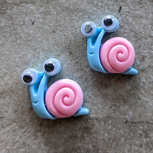 May include: Two blue and pink snail shaped buttons with googly eyes.