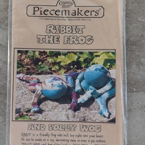 May include: A clear plastic bag containing a sewing pattern for a frog toy. The pattern is titled "Ribbit the Frog" and features two plush frogs in shades of blue and patterned fabric. The "Piecemakers" logo is at the top.