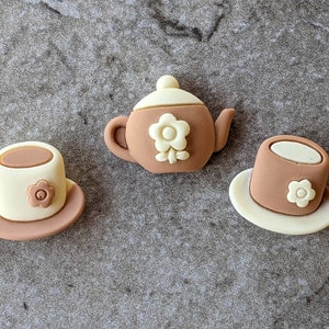 May include: Three brown and white ceramic teacup and teapot figurines with a flower design.