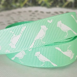 May include: A light green ribbon with a white bird design. The ribbon is folded in half and the design is visible on both sides.