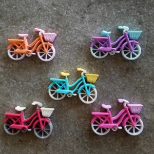 May include: Five miniature toy bicycles in different colors, including pink, blue, purple, and orange. Each bicycle has a small basket on the front and white wheels.
