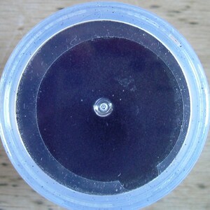 May include: A close-up view of a clear plastic container with a black circular lid. The lid has a small hole in the center.