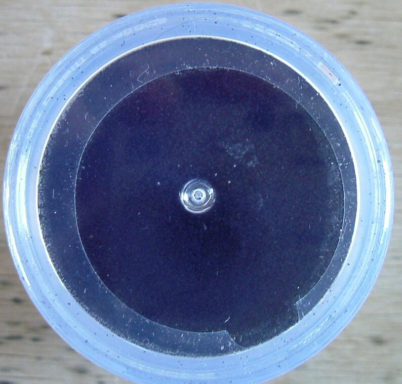 May include: A close-up view of a clear plastic container with a black circular lid. The lid has a small hole in the center.