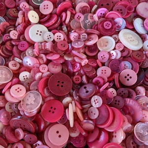 May include: A large collection of pink and white buttons of various sizes and styles. The buttons are made of plastic and have a smooth, shiny finish.