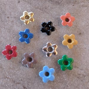 May include: A collection of flower-shaped knobs in various colors, including gold, black, red, blue, and green. These decorative knobs have a glossy finish and a central hole, suitable for furniture or craft projects.