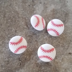 May include: Four white baseball-themed buttons with red stitching. The buttons are round and have a raised design.