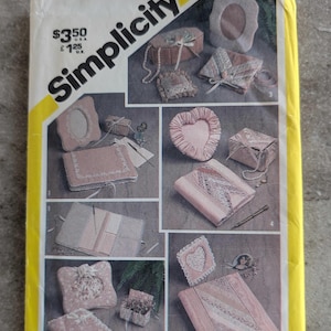 May include: A vintage Simplicity sewing pattern envelope, featuring various craft projects. The envelope is yellow and white, with the Simplicity logo and the number 5296. The projects include a heart-shaped pillow, a photo frame, and small boxes.