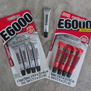 May include: Two blister packs of E6000 adhesive, each containing four 0.18 fl oz tubes, and one loose 0.18 fl oz tube. The left pack features silver tubes, while the right pack contains red tubes. Both packs display the E6000 logo and product details.