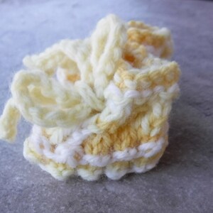 May include: A pair of crocheted baby booties in yellow and white. The booties have a simple design and are tied with a ribbon.