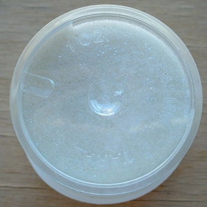 May include: A clear plastic container with a white, glittery substance inside. The container has a label that reads "1/16 oz."