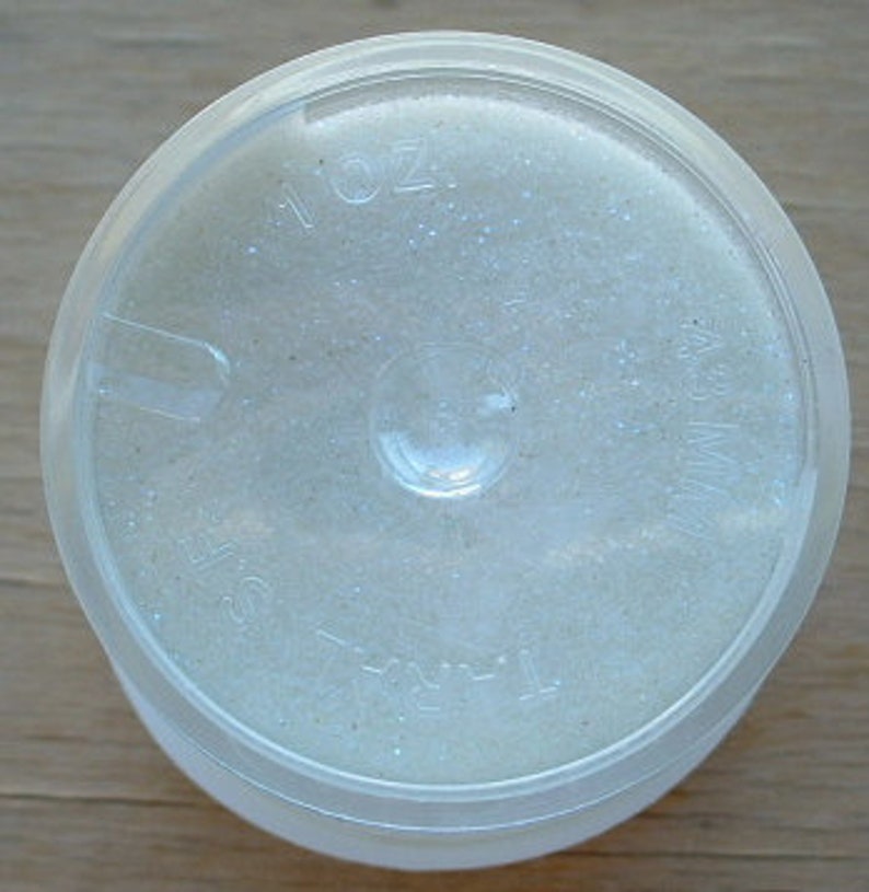 May include: A clear plastic container with a white, glittery substance inside. The container has a label that reads "1/16 oz."