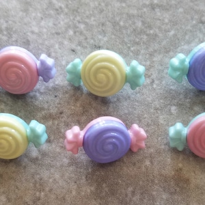 May include: Six pastel-colored candy buttons with a swirl design. Each button has a light blue wrapper with a white star on each end.