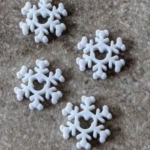 May include: Four white snowflake-shaped ornaments with a heart-shaped cutout in the center. The ornaments are made of a smooth, white material and have a slightly raised texture.