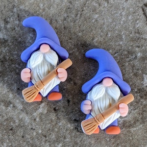 May include: Two purple gnome figurines with white beards and hats. Each gnome is holding a brown broom.