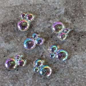 May include: A collection of iridescent soap bubbles of various sizes and shapes on a textured gray surface.