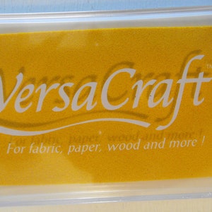 May include: A yellow ink pad with the text "VersaCraft" in white lettering. The ink pad is in a clear plastic case and has the text "For fabric, paper, wood and more!" in white lettering.